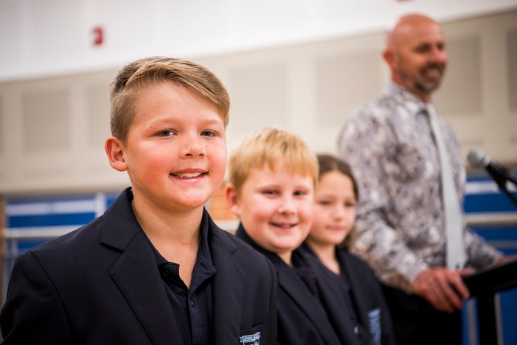 Three students stand with the Principal smiling on stage