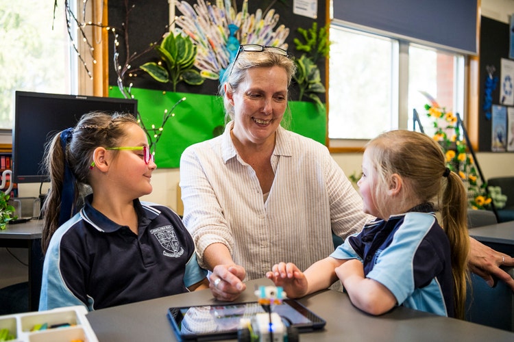 A teacher smiling with two young students who are exploring the digital resources in the library.