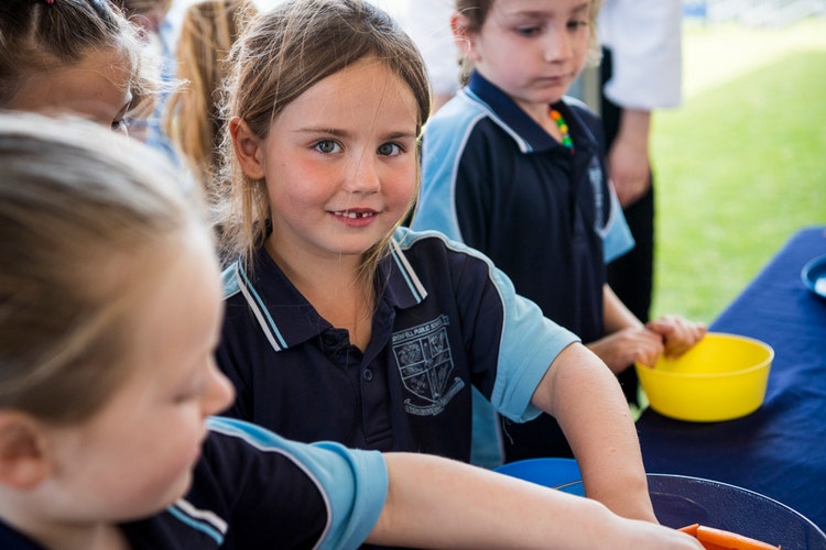 A young girl is smiling while reaching for some fruit.