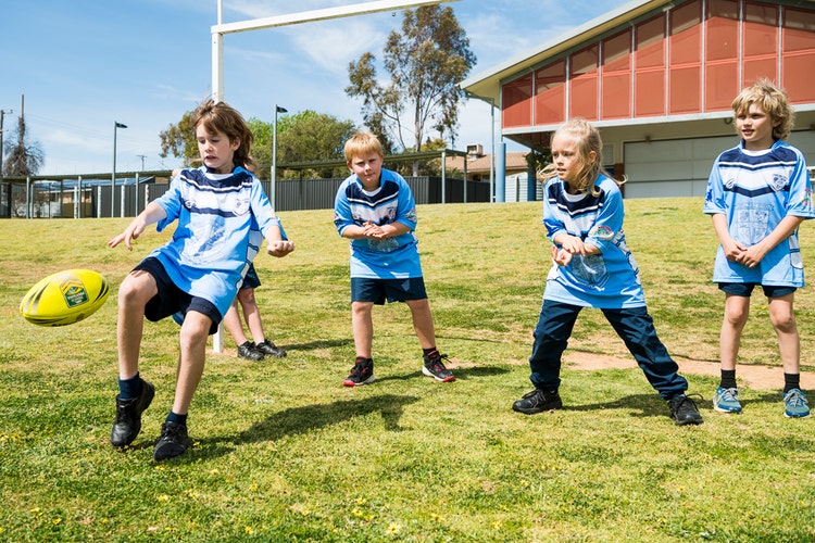 Four students on the sports oval, one is kicking a football.